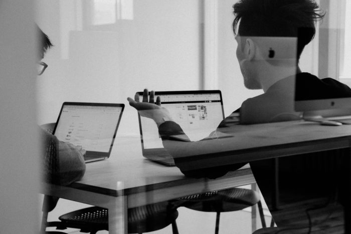 Two professionals reviewing pension documents on laptops during a meeting